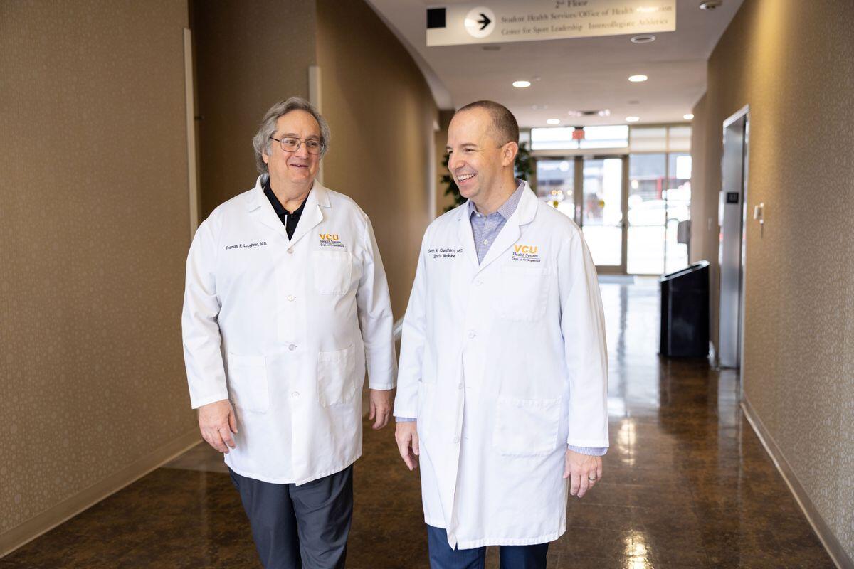Two men wearing white doctor's coats walking down a hallway. 