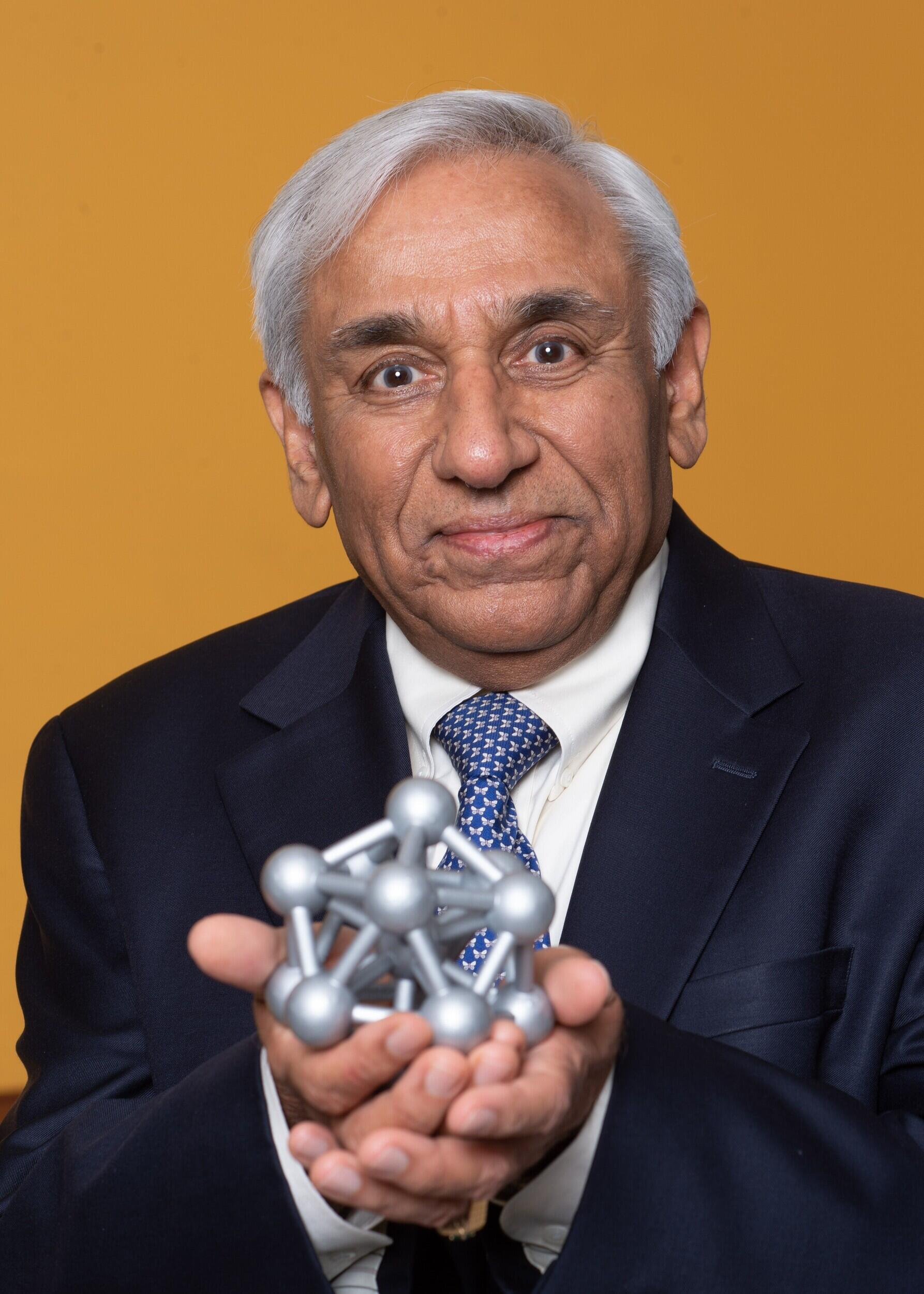 A photo of a man in a suit and tie holding a model of an atom. 