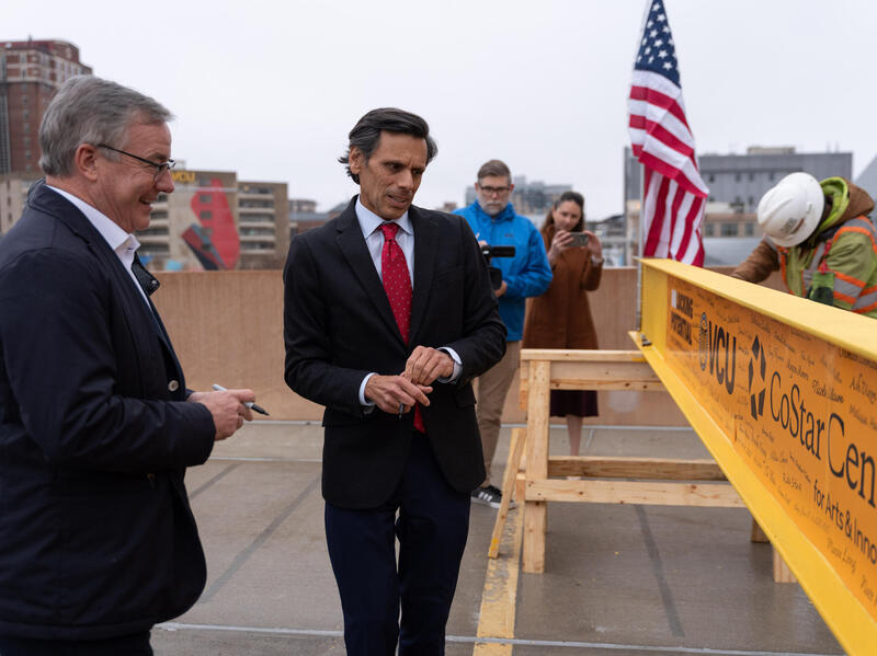 A photo of two men standing next to a yellow construction beam. 