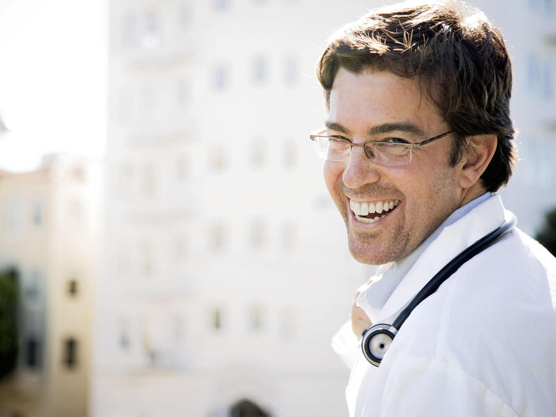 A photo of a man from the shoulders up. He is looking over his right shoulder and smiling. 