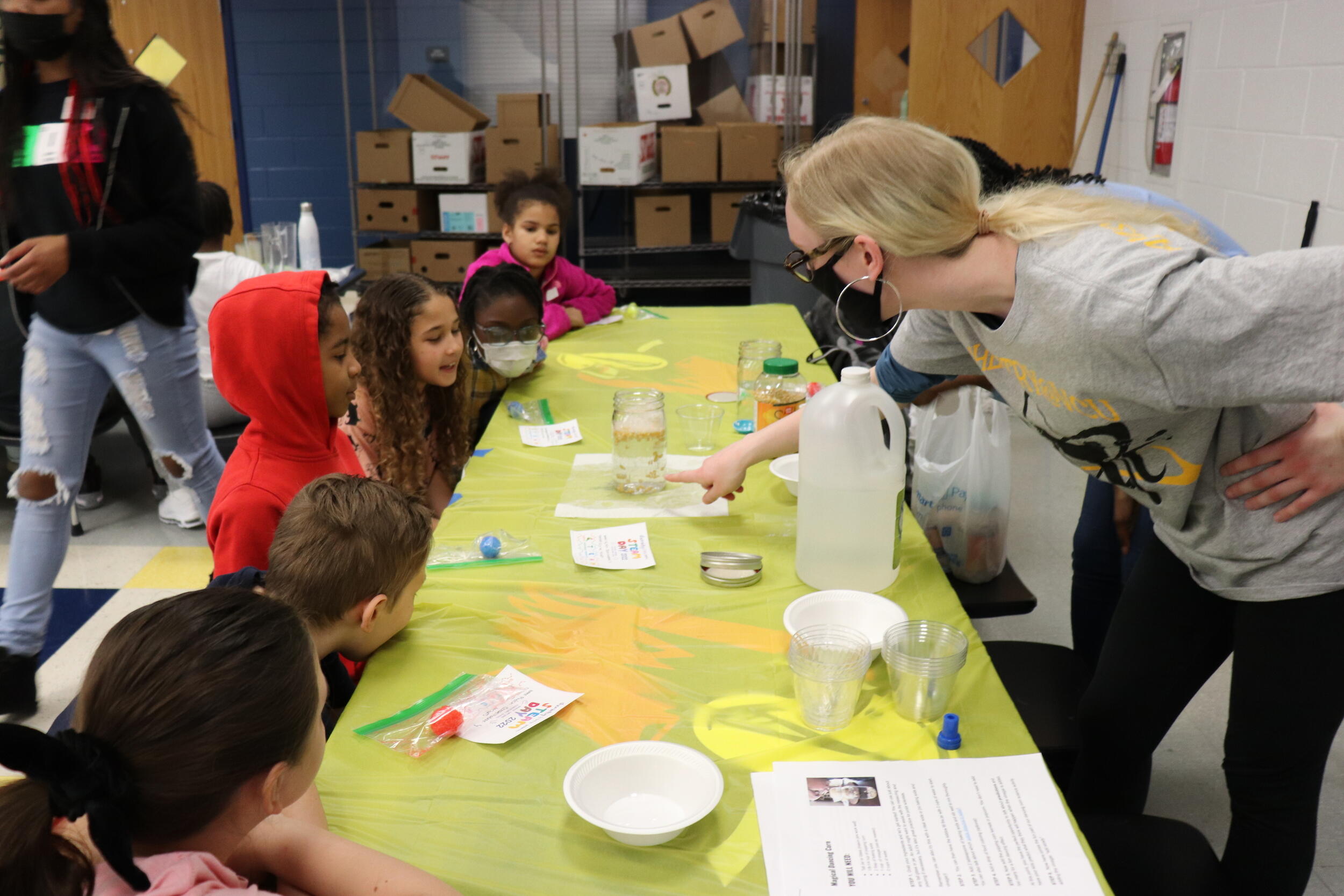 A VCU student showing elementary school students a jar filled with corn, baking soda, water, and vinegar