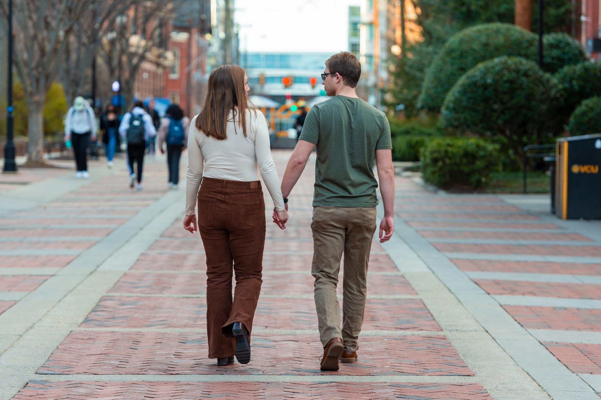 A couple holding hands while walking down VCU's Shafer Court.
