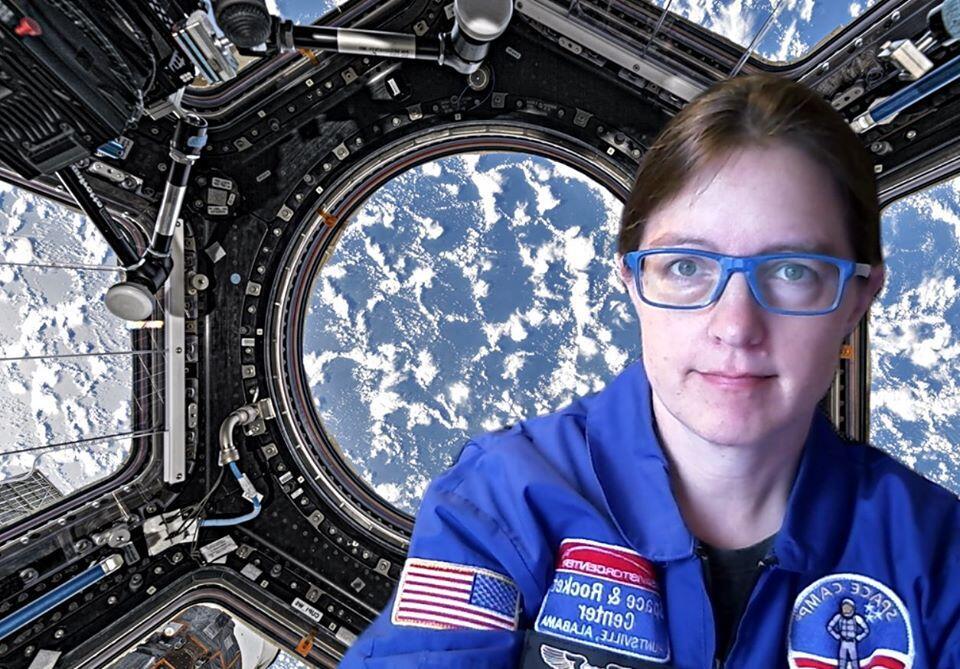 A teacher dressed in a blue jacket with a background looking out the windows of a space station pointed toward Earth.