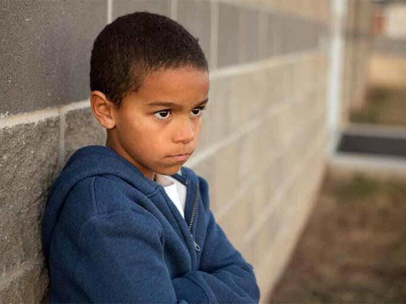 A little boy in a hoodie leaning against a gray stone wall. 