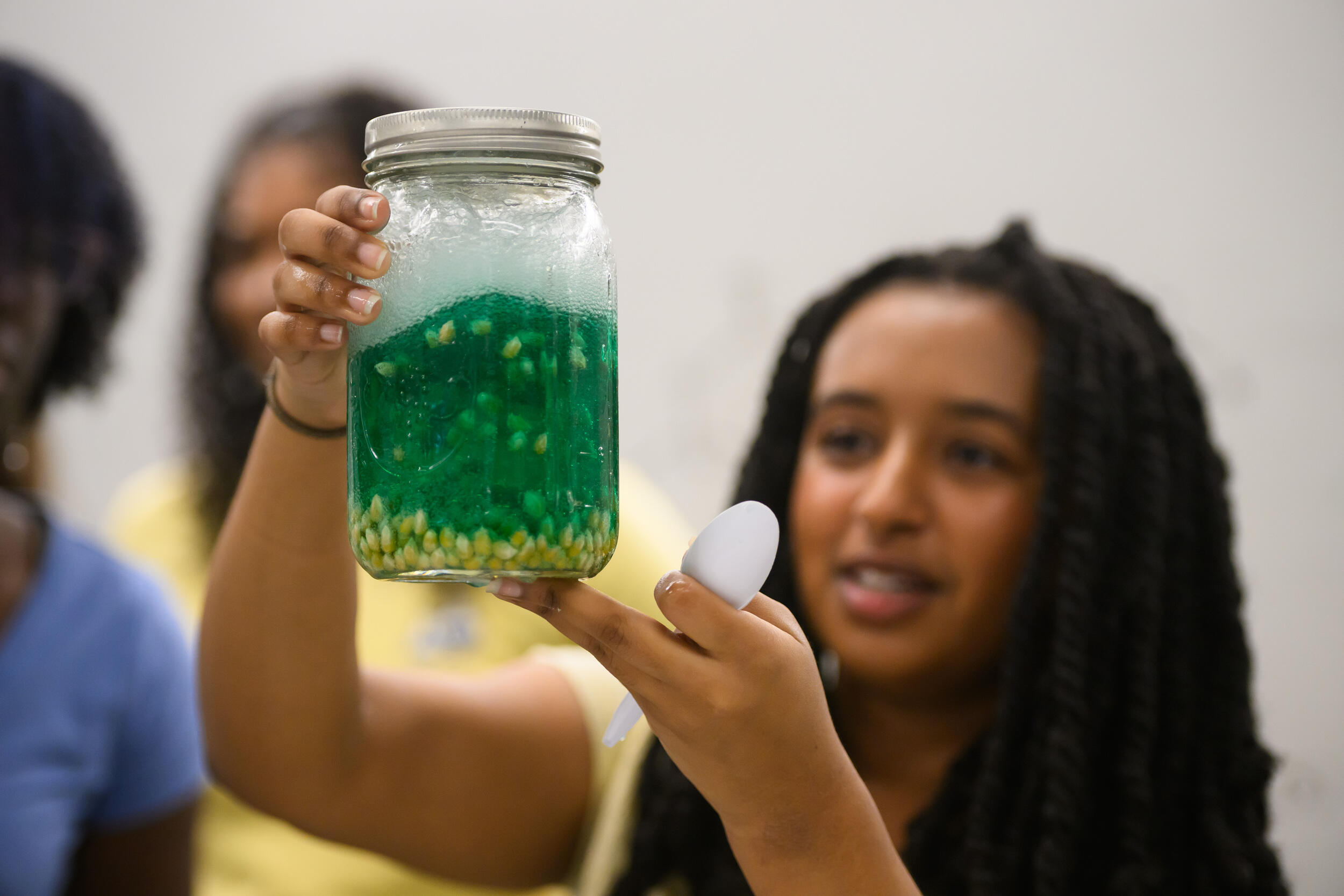 A photo of a woman holding a jar filled with green liquid and corn kernels. 