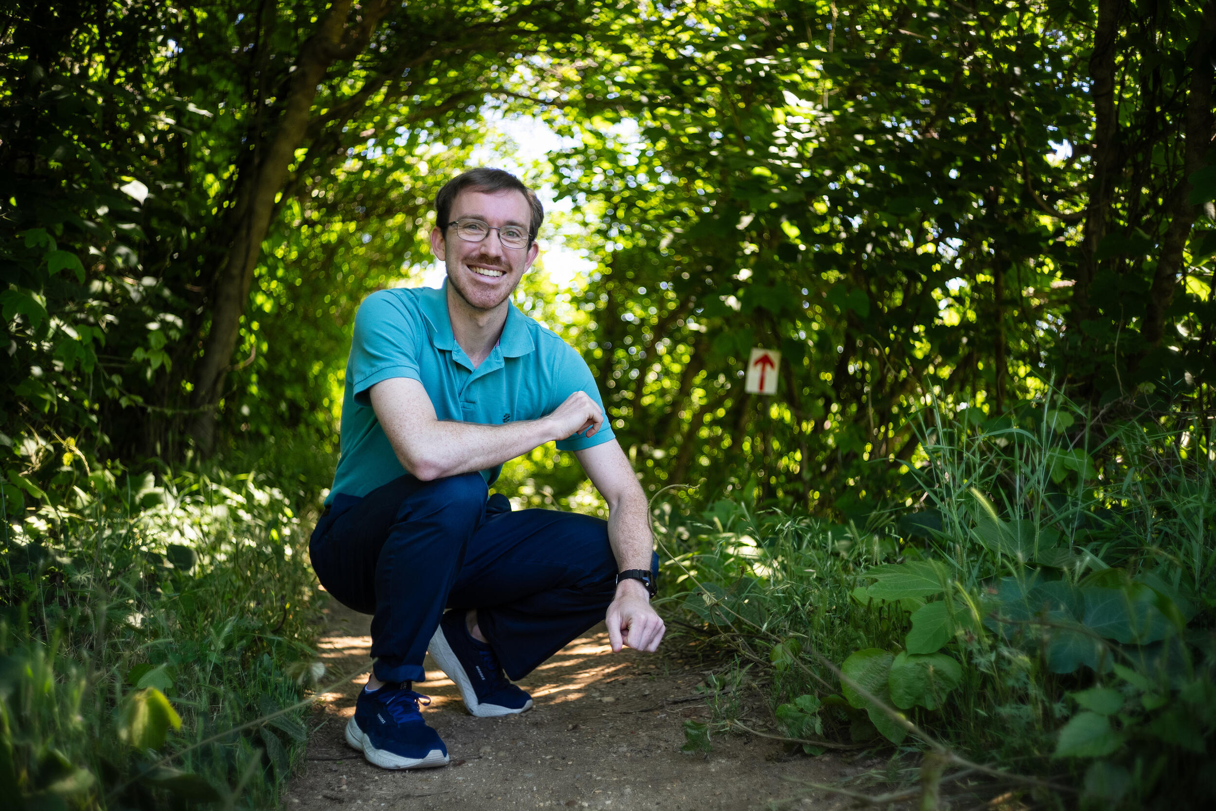 A photo of a man kneeling on a path in the woods. 