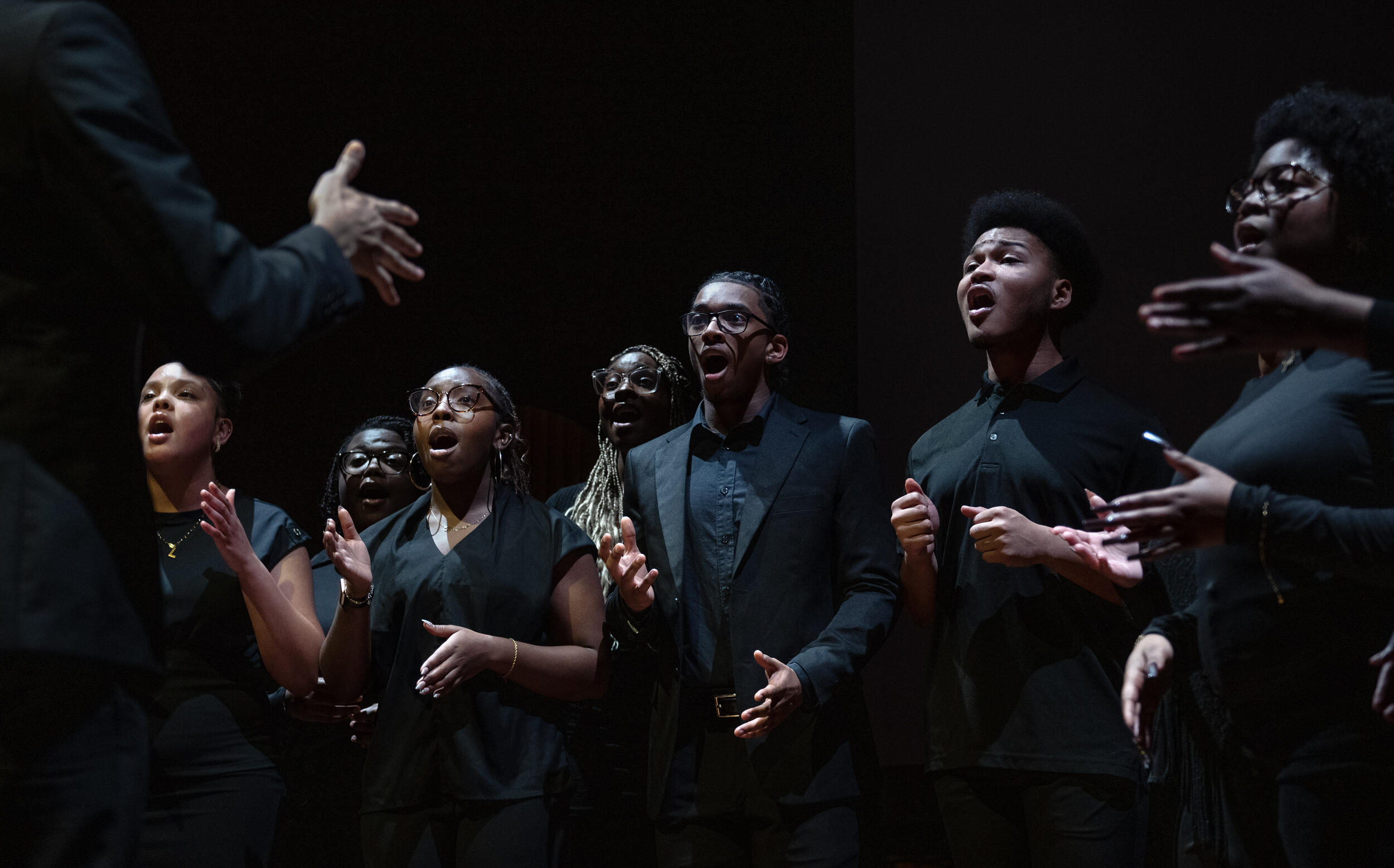 A chorus of people wearing all black singing. 