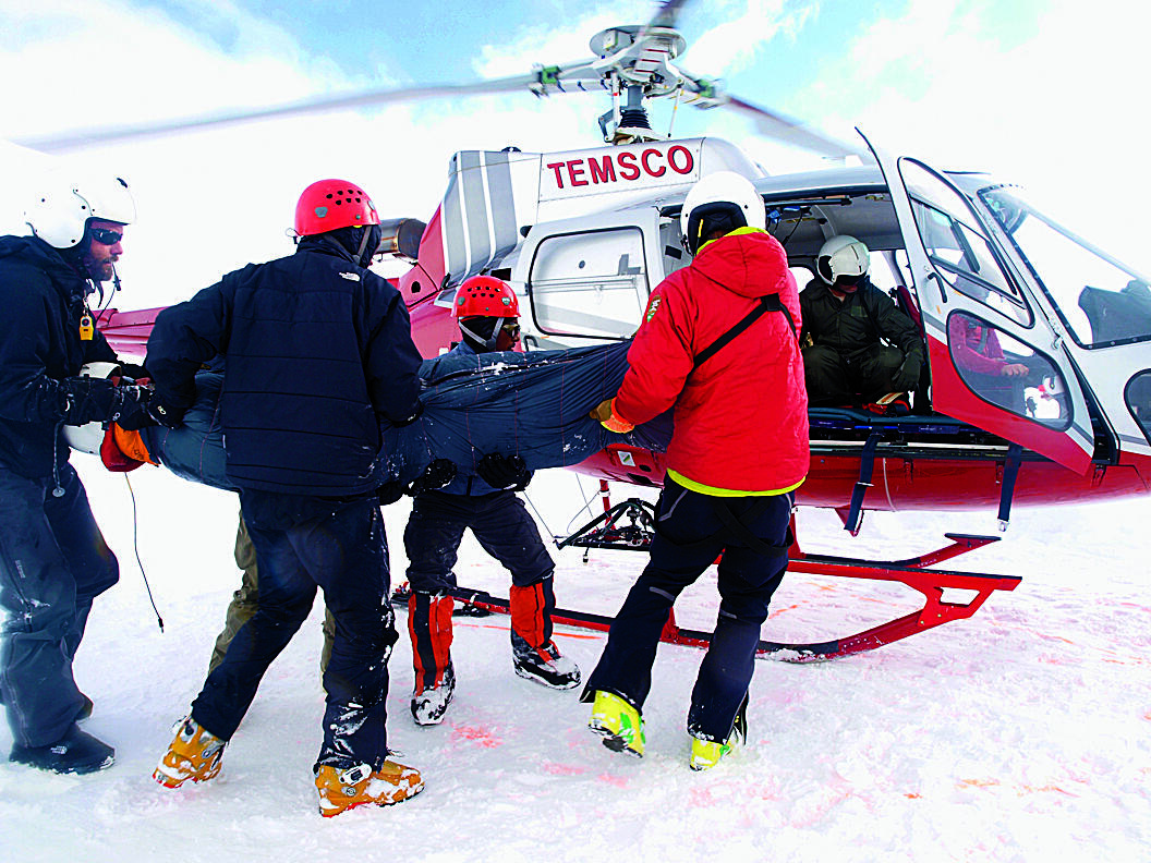 Four people carrying another person into a helicopter in the snow. 