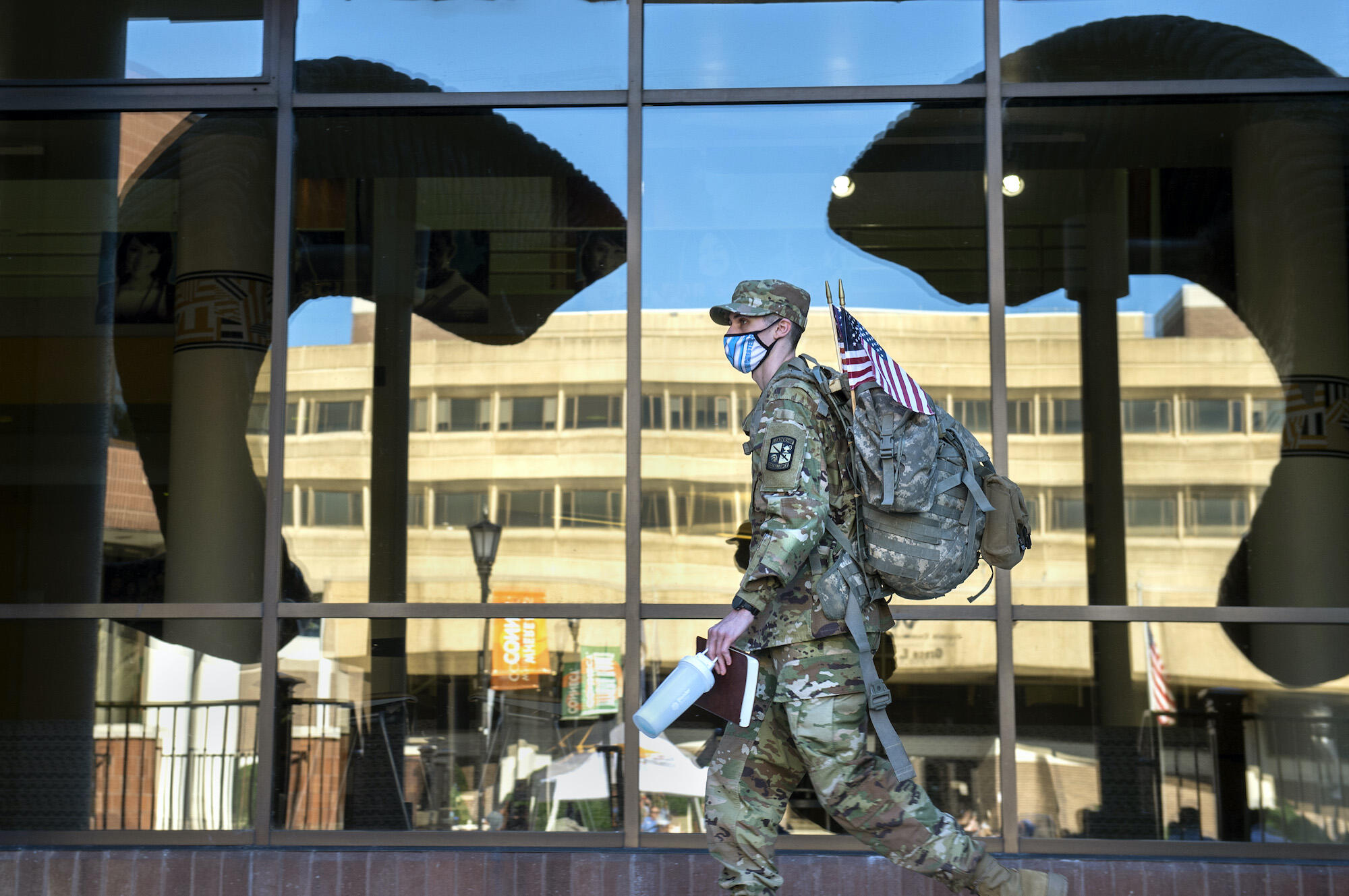 A photo of a man wearing a military uniform walking past a window with a reflection of ram horns on it. 