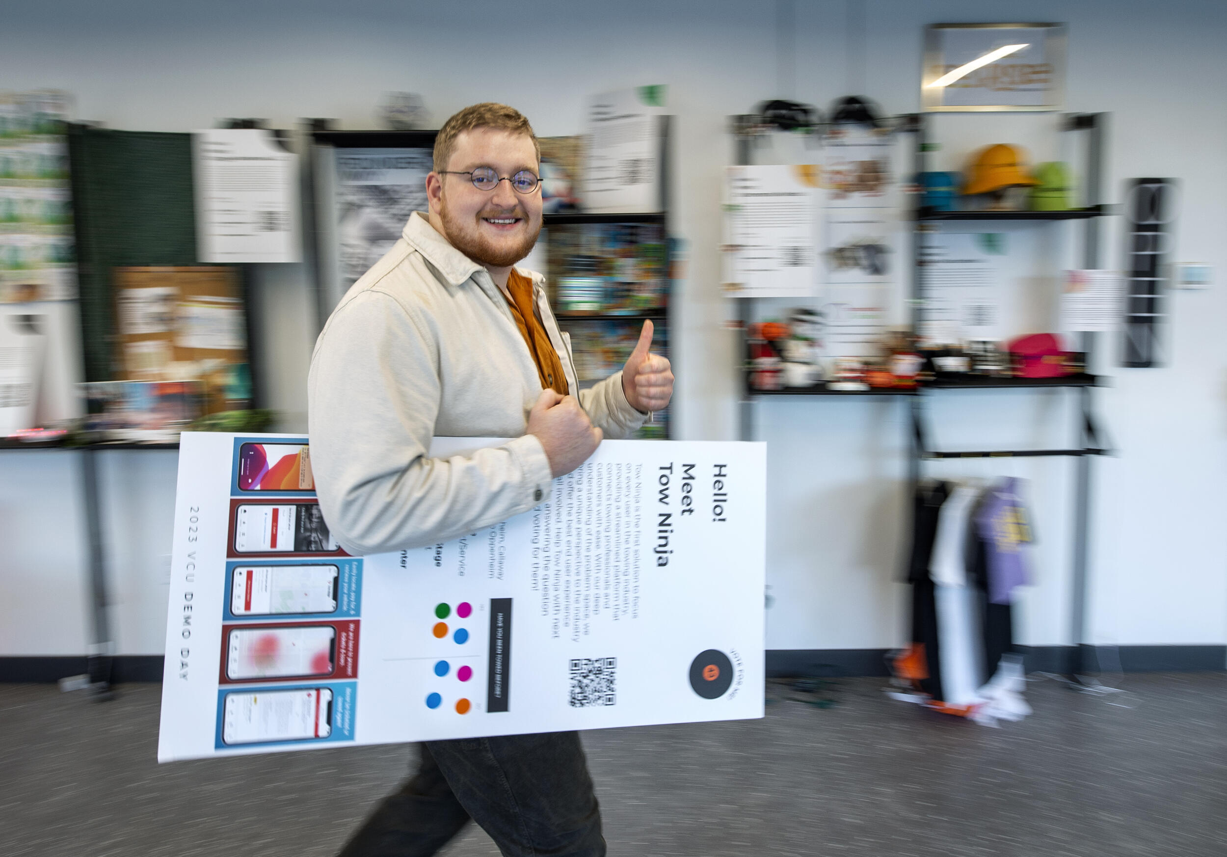 A photo of a man walking with a poster under his arm while giving a thumbs up 
