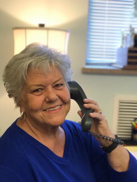 A smiling woman holding a telephone receiver to her right ear.