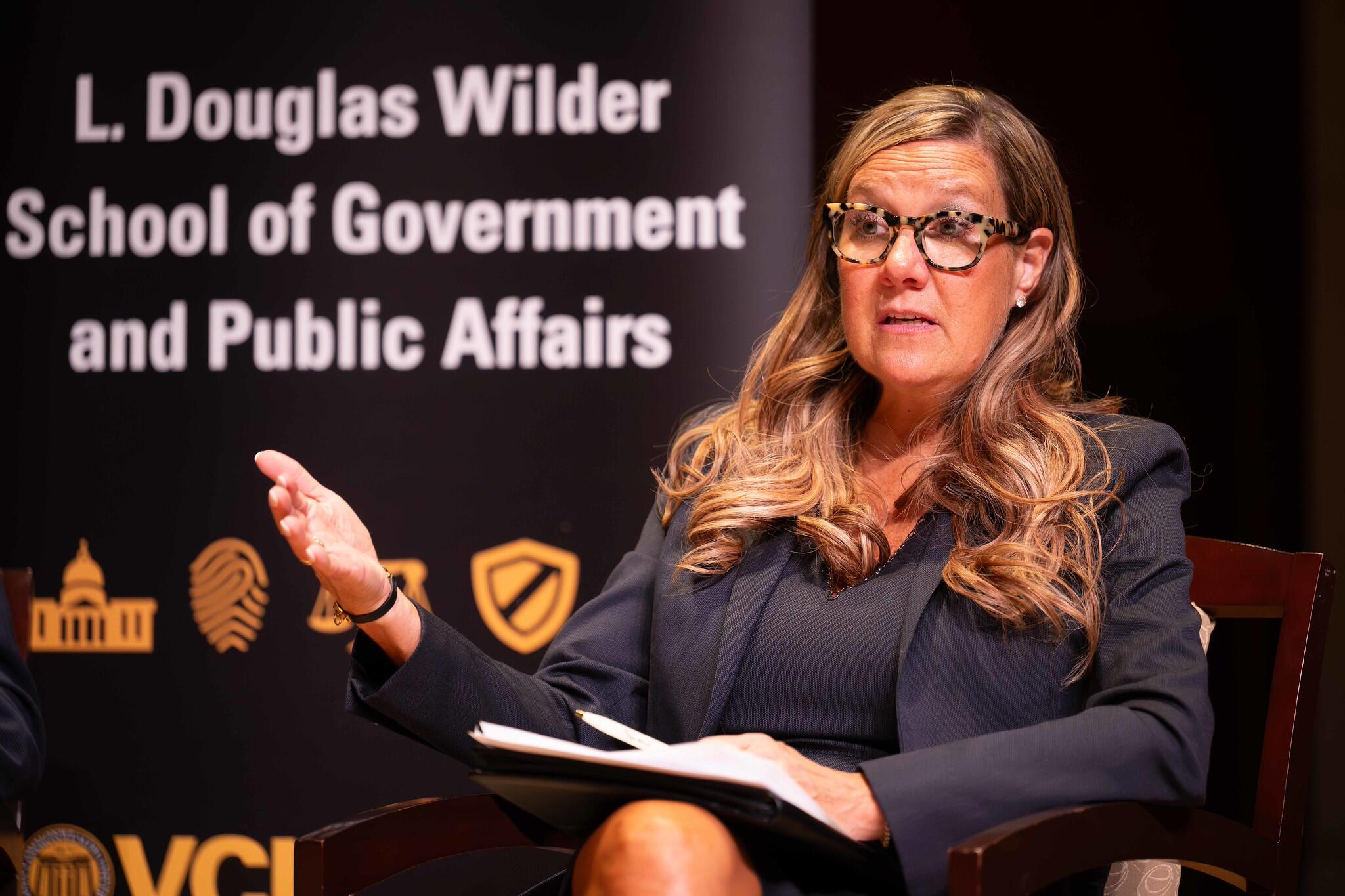Robyn McDougle speaks at an event. Behind her are the words: L. Douglas Wilder School of Government and Public Affairs.