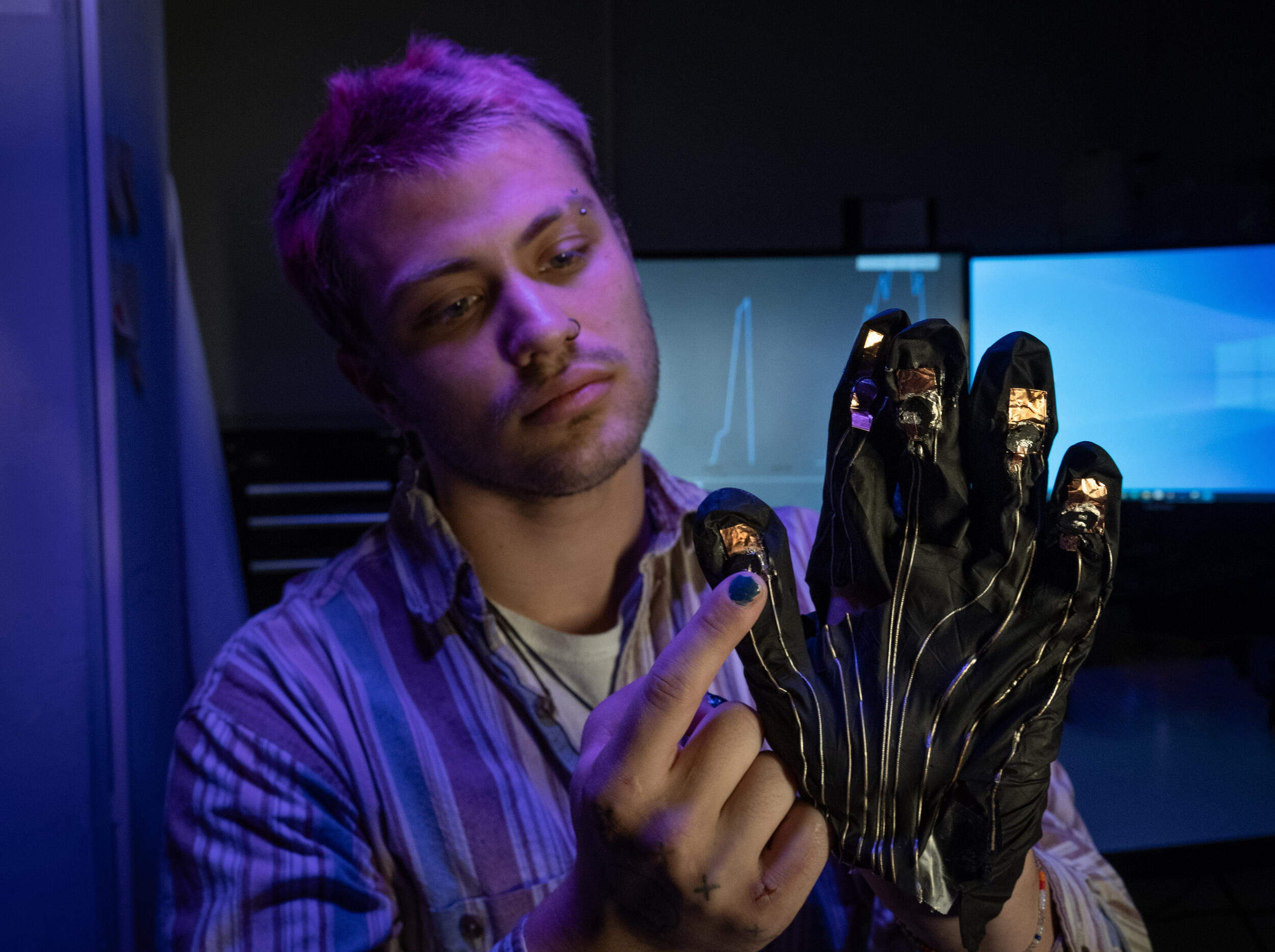 A photo of a man wearing a black glove with metallic wires on it, on his right hand. His left index finger is touching his right thumb.