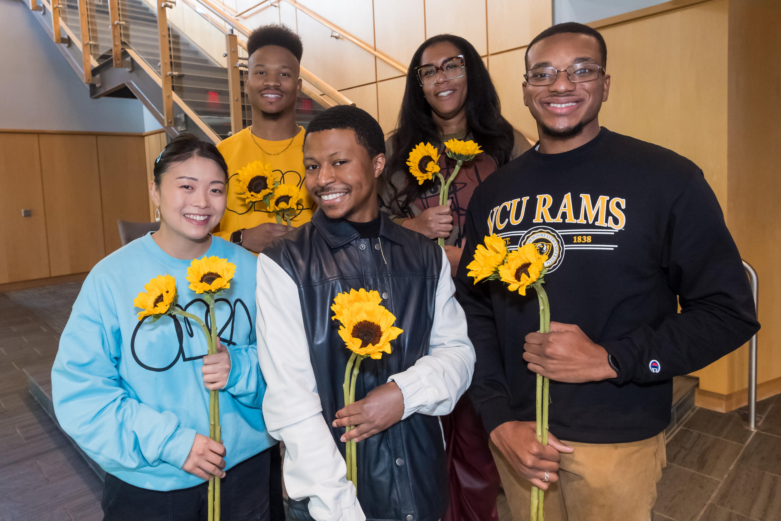 A photo of five people holding sunflowers. 