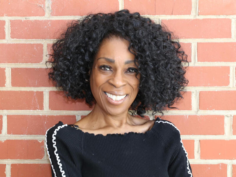 A woman in a black stop smiles in front of a brick wall.