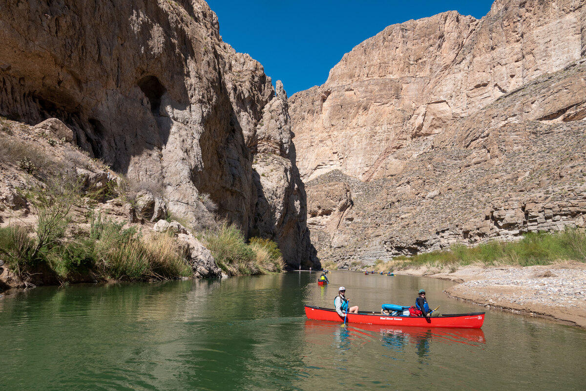 People in a red canoe on a river in the middle of two cliffs. 