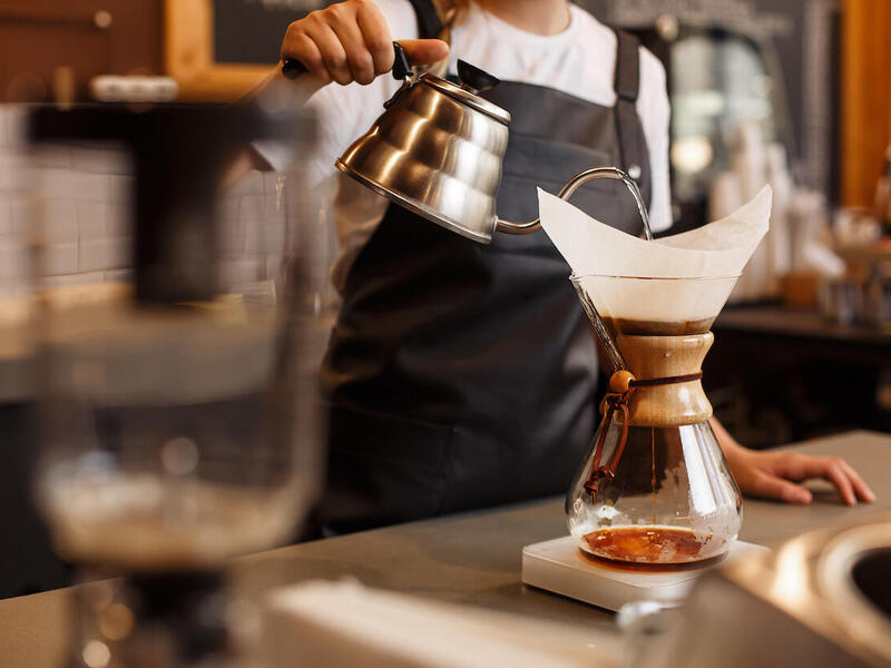 A barista brewing coffee by pouring water from a kettle into a paper filter.