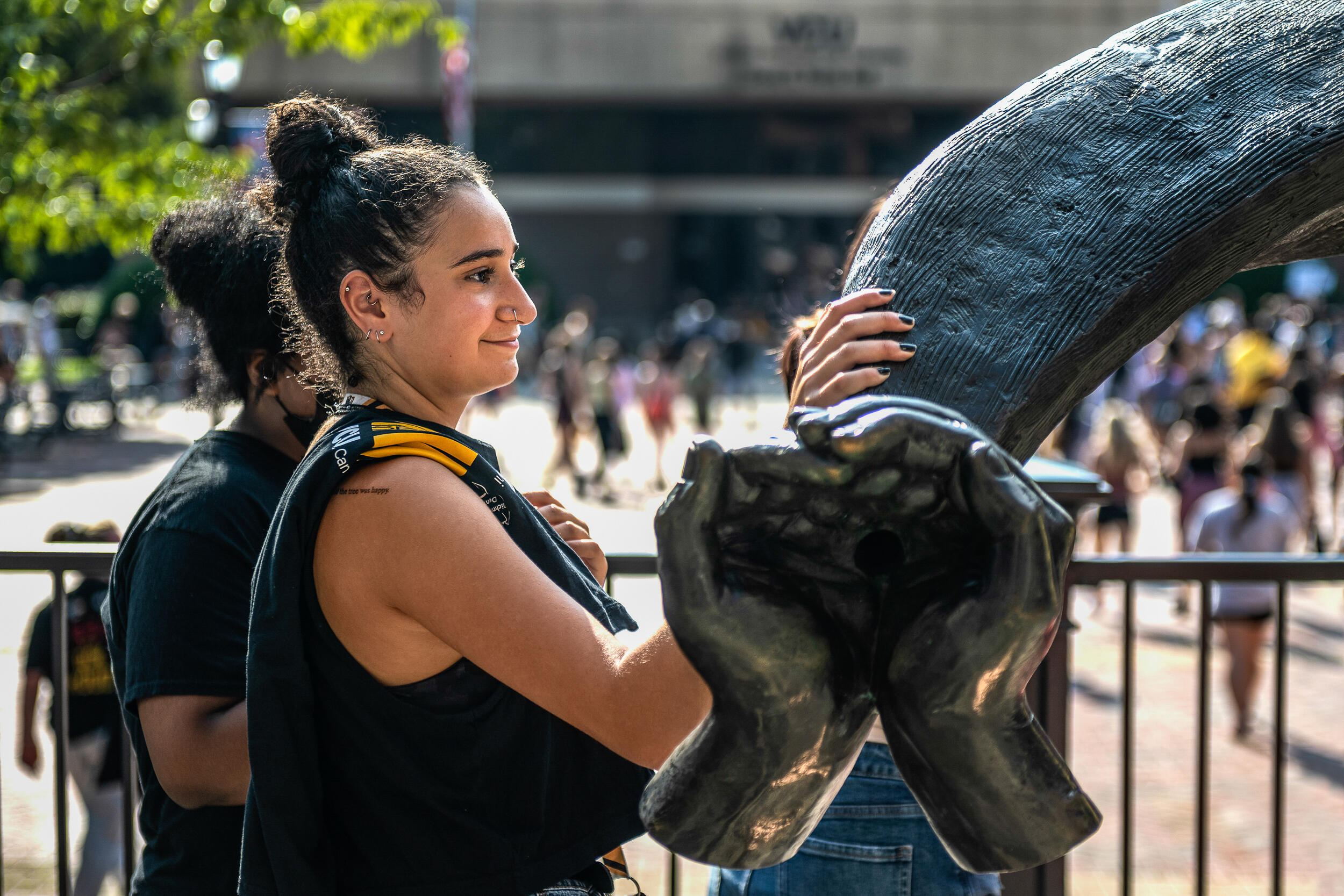 A student rests a hand on the Ram Horns outside The Commons in front of a plaza.