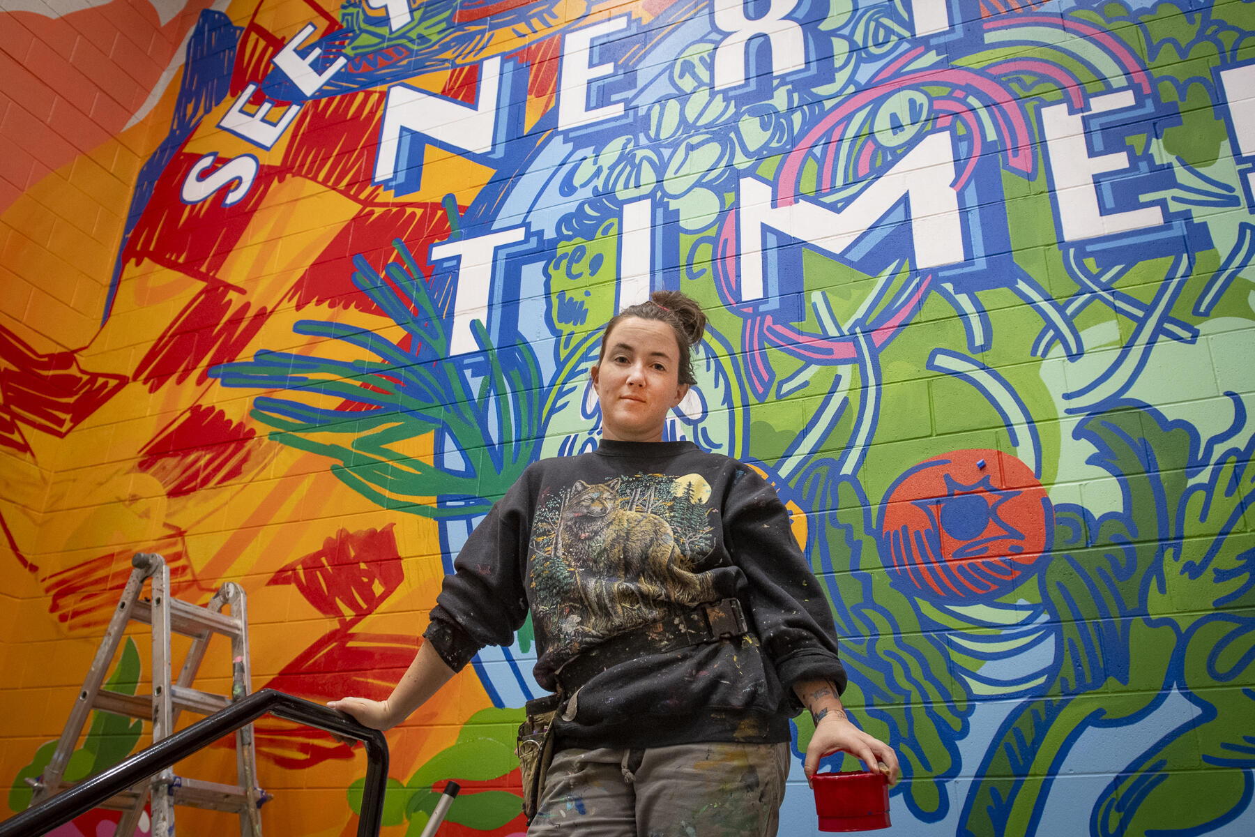 A photo of a woman standing in front of a mural. 