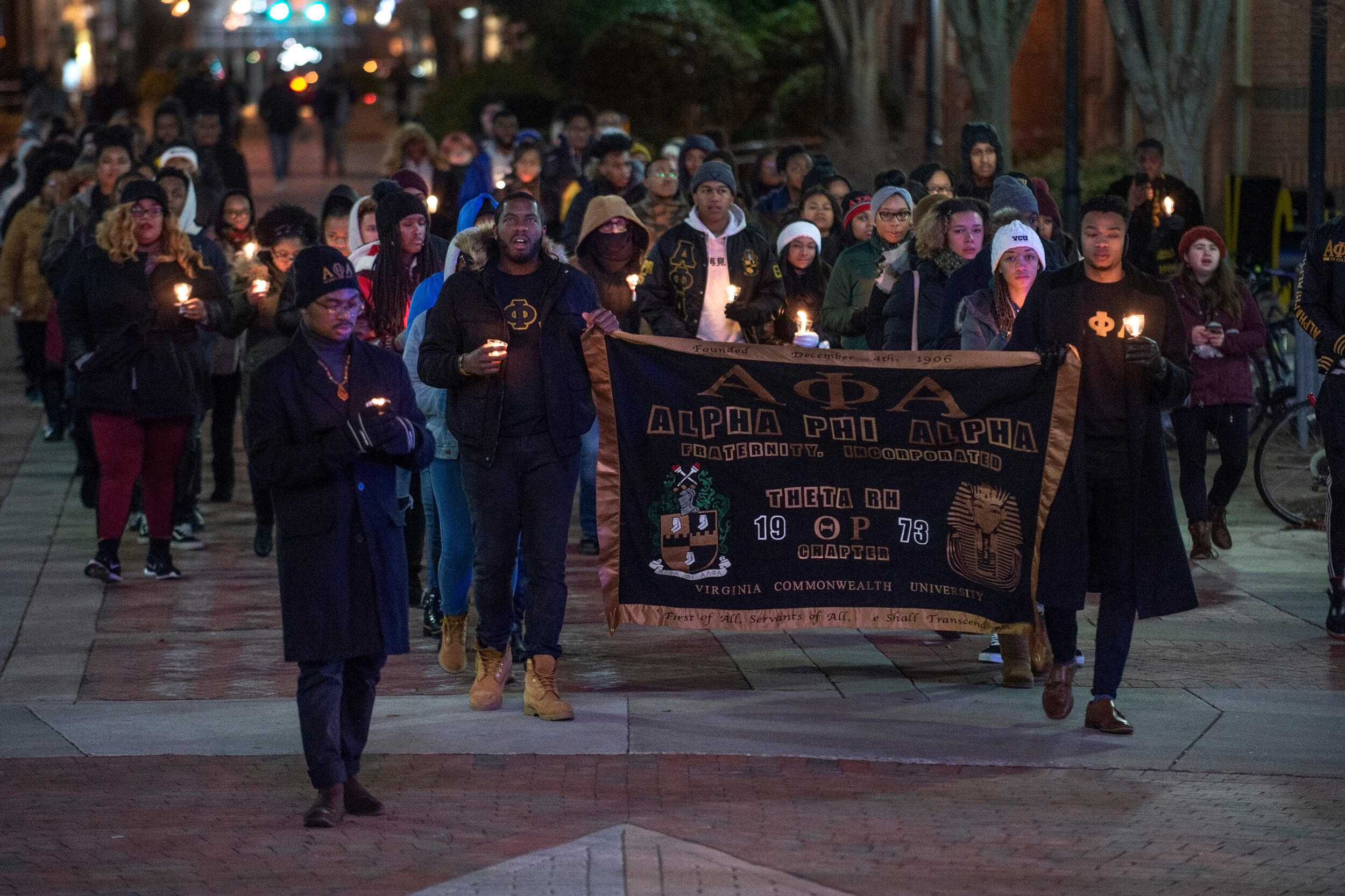 A group of people walk together at night holding lit candles.