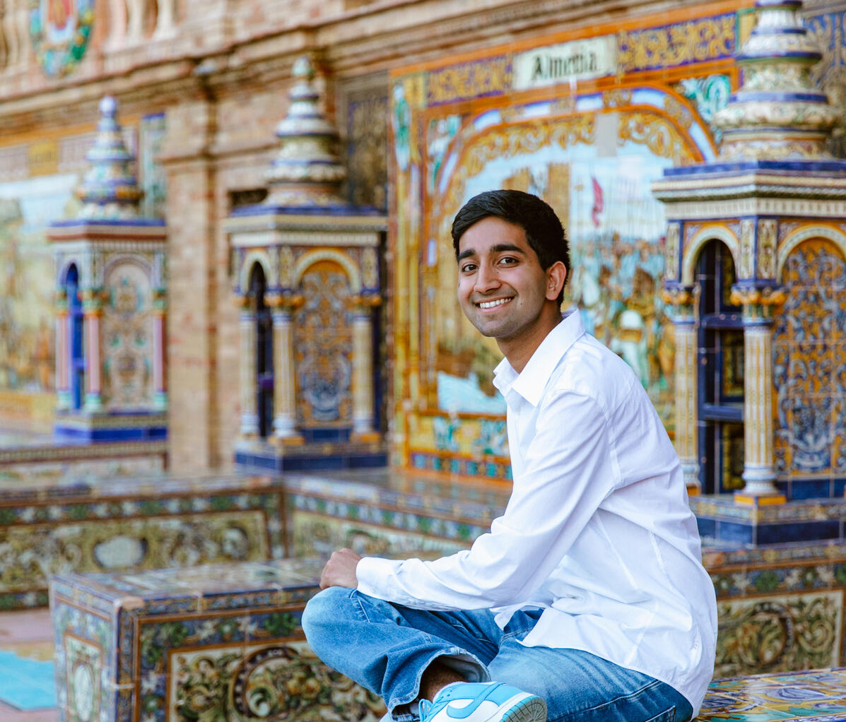 A man wearing a white long sleeve shirt and blue jeans sitting on a mosaic tile cube 