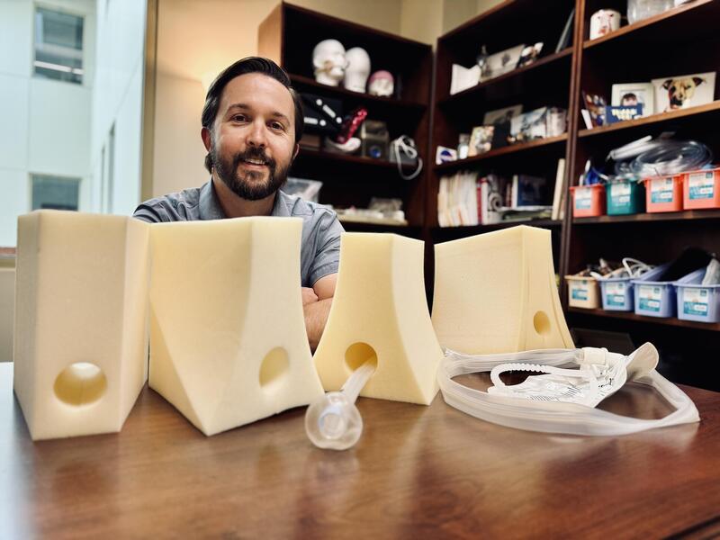 A photo of a man sitting at a table with four pastic devices sitting in front of him. 