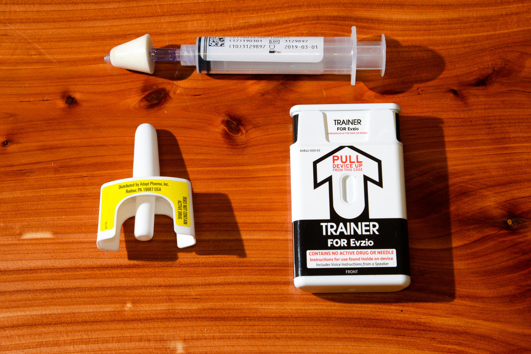 Three varieties of naloxone training devices sit on a wood table.

