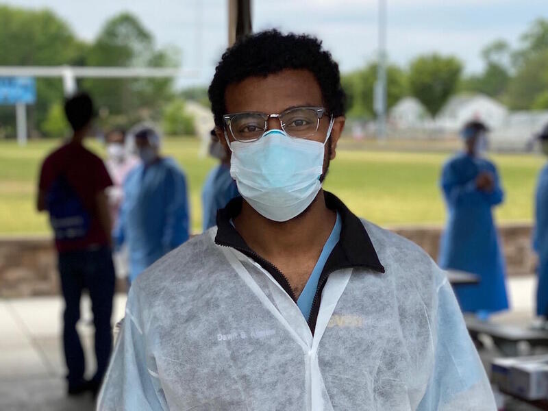 A person wearing a pair of glasses, a mask and medical scrubs.