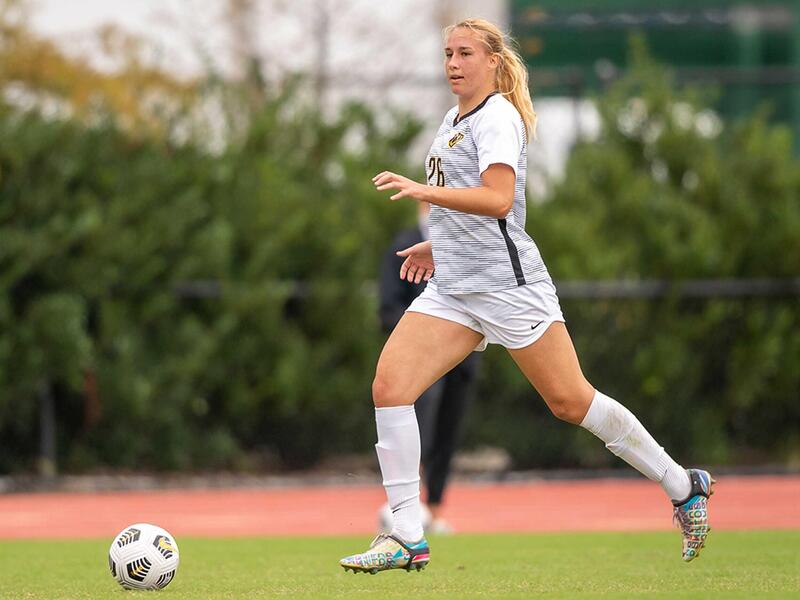 A woman running on a soccer field towards a soccer ball