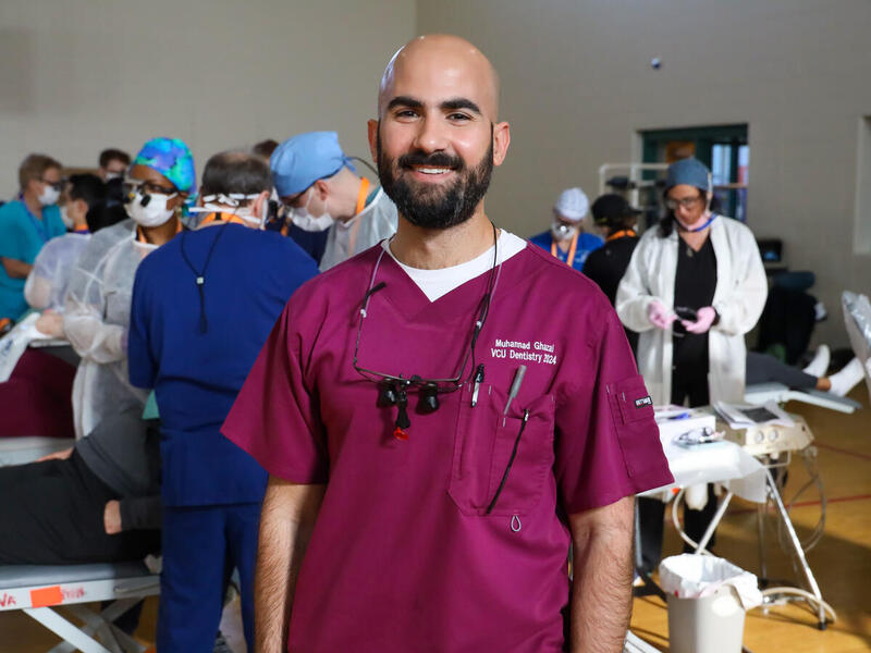 A photo of a man wearing dental scrubs standing in a room full of dentists. 