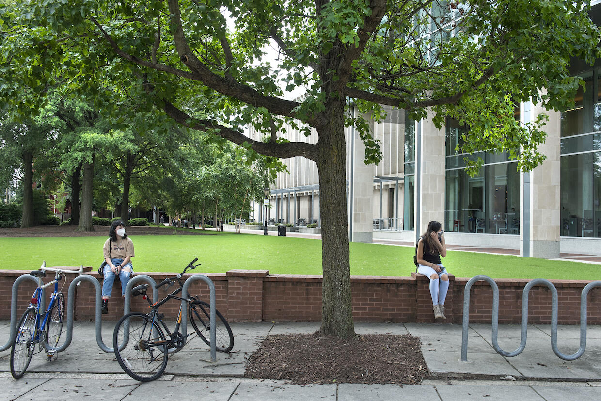 Two students sit far apart on a low brick wall on the VCU Monroe Park Campus.