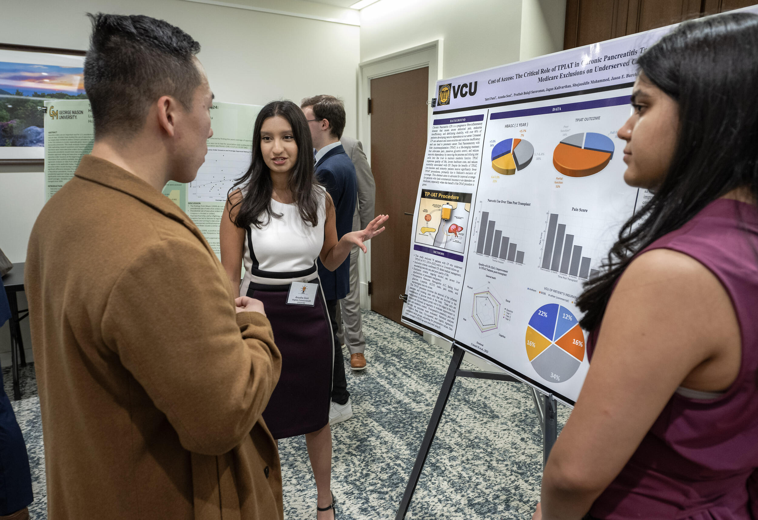 A photo of two women standing on either side of a posert with research on it. THere is a man standing in front of the poster who is listening to the woman on the left speak. 