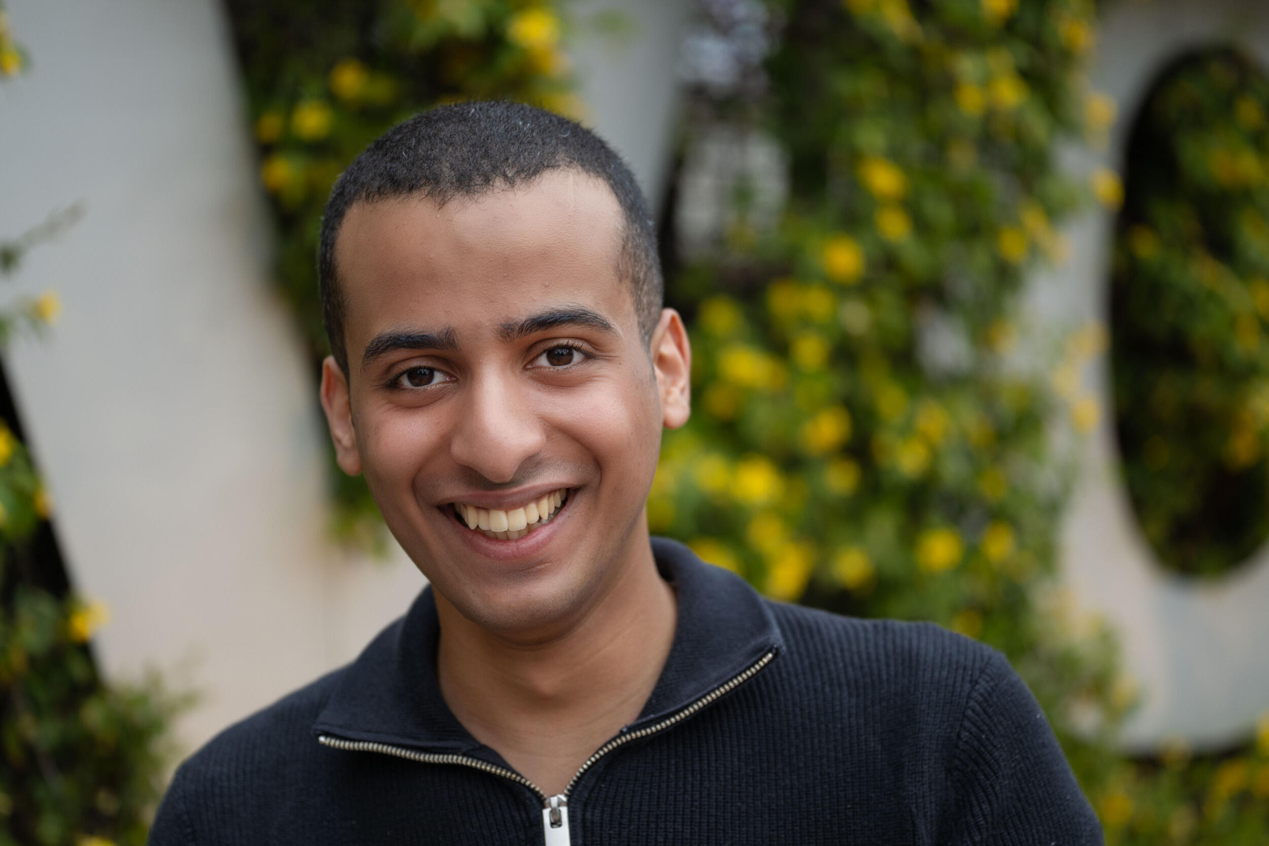 A man in a dark zip-up shirt smiles.