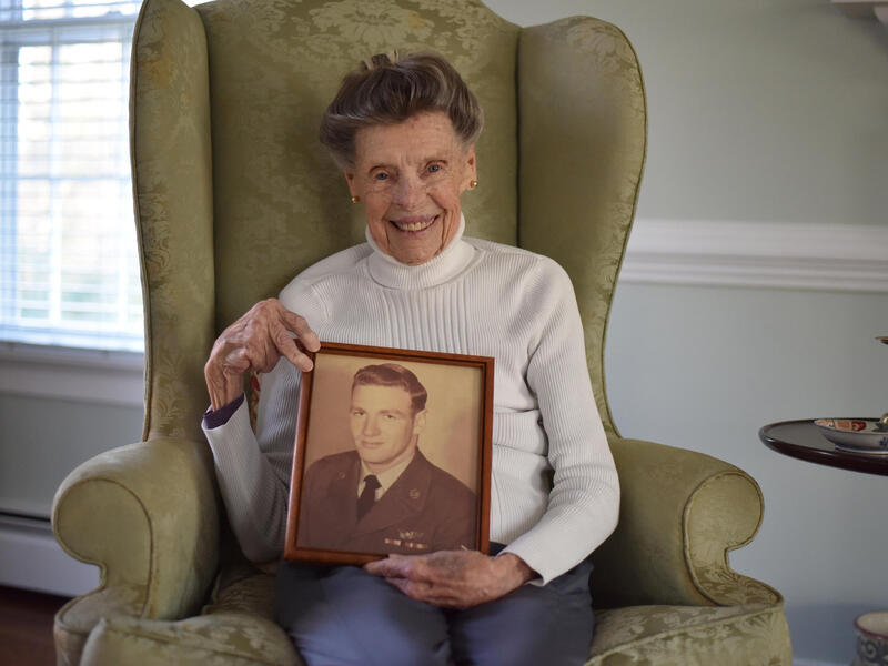 A photo of an old woman in a chair holding a sepia tone photo of a man in a military uniform. 