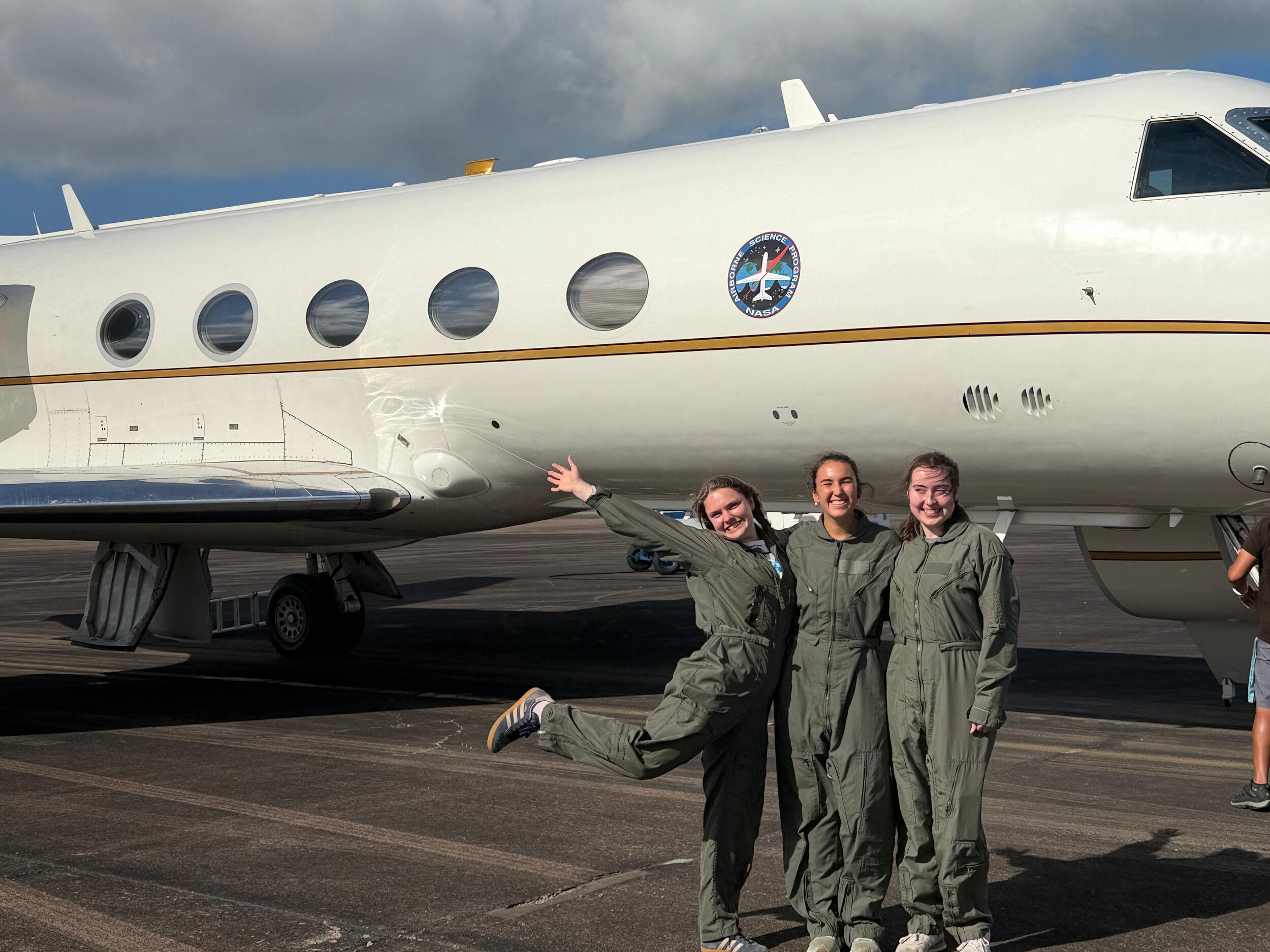 A group photo of three women standing in front of an airplane. 