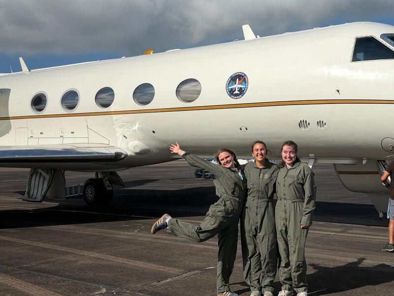 A group photo of three women standing in front of an airplane. 