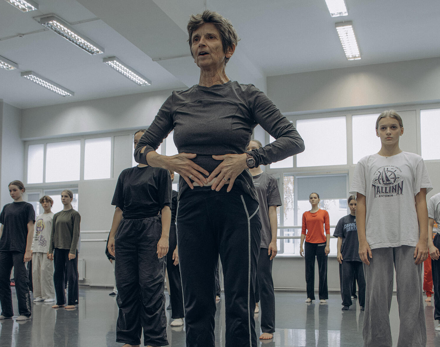 A photo of a woman standing in the front of a dance studio. Behind her several other people are standing