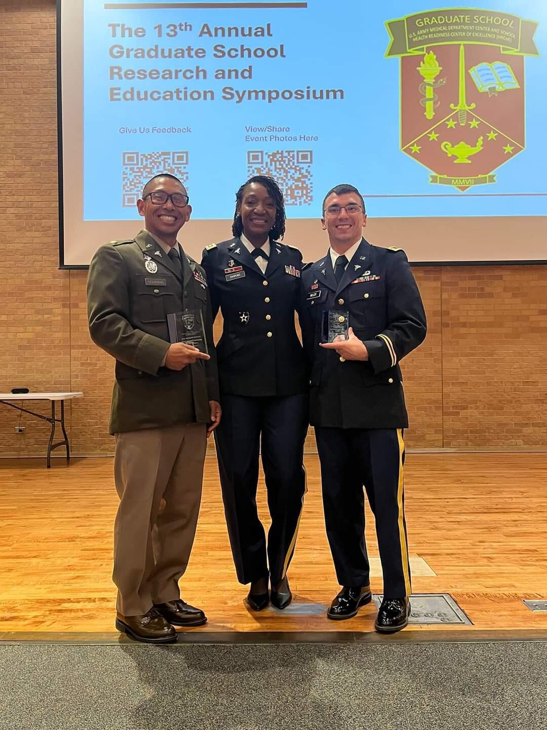 A photo of three people in formal military unifroms standing and smiling. 