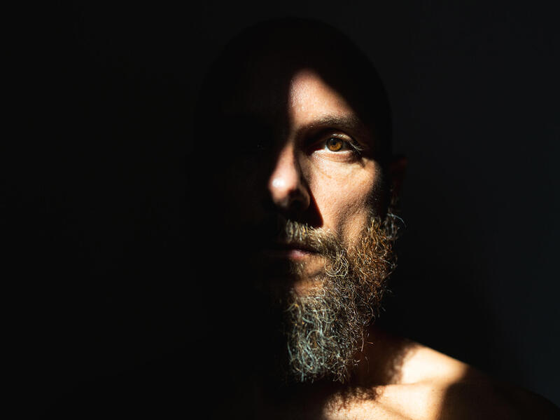 A photo of a man's face that is more than halfway covered in shadow. 