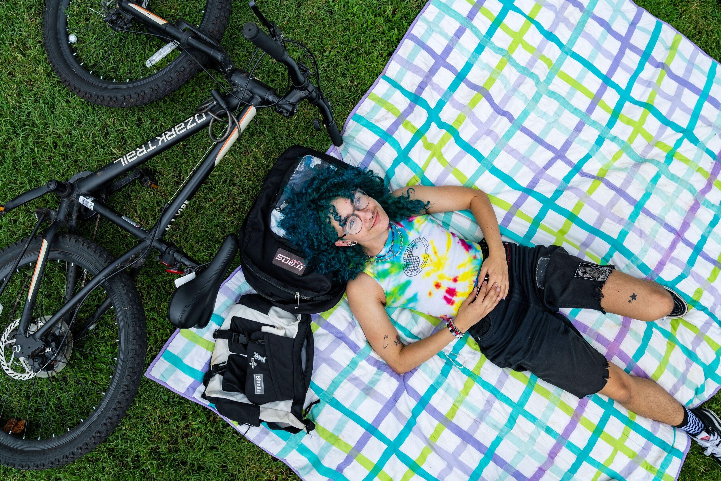 A view from above of a person lying on a blanket in the grass with a bicycle on the ground near their head.