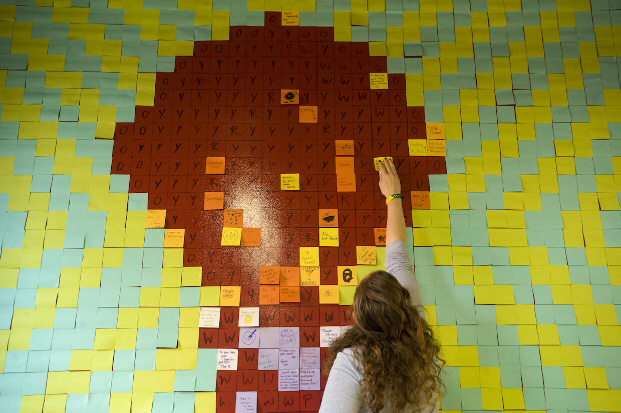A person applies a sticky note on grid of other similar pieces of paper.