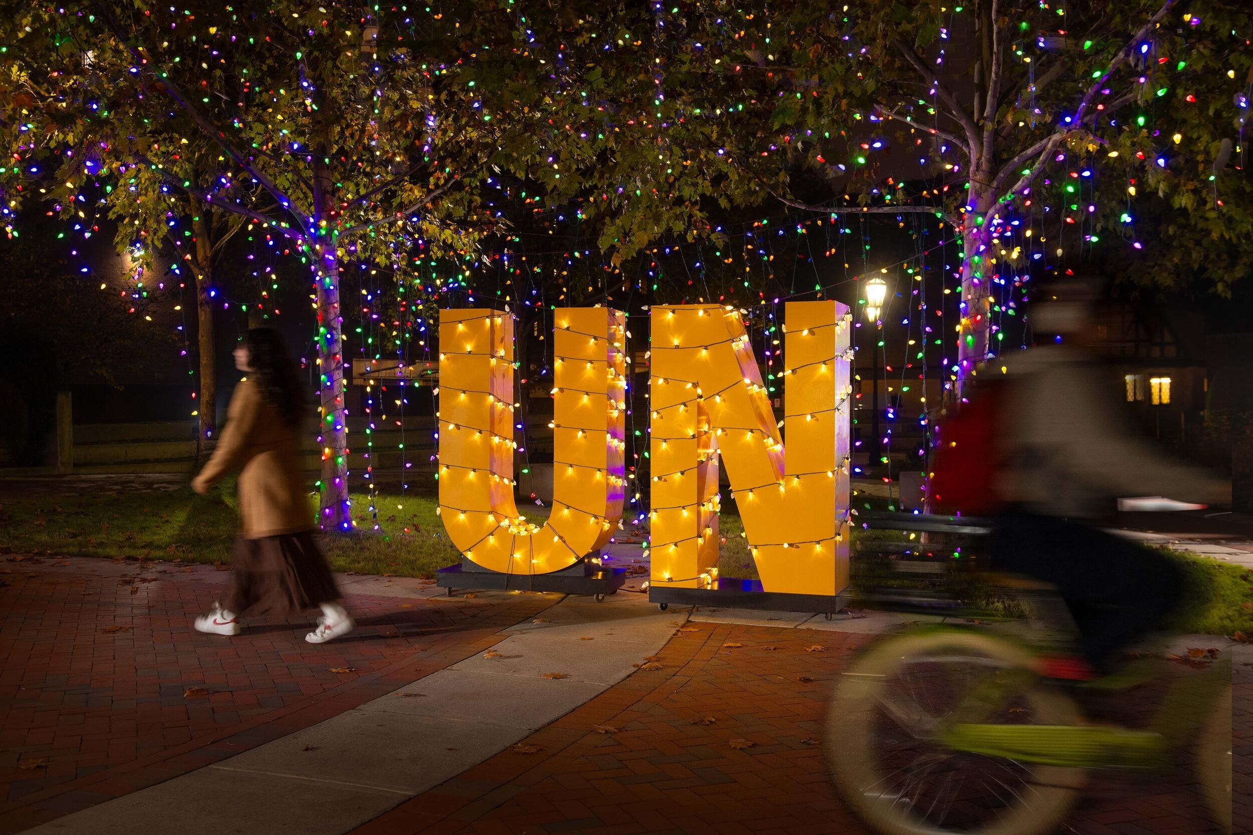 A gold sign of the letters UN is lit by holiday lights at night.