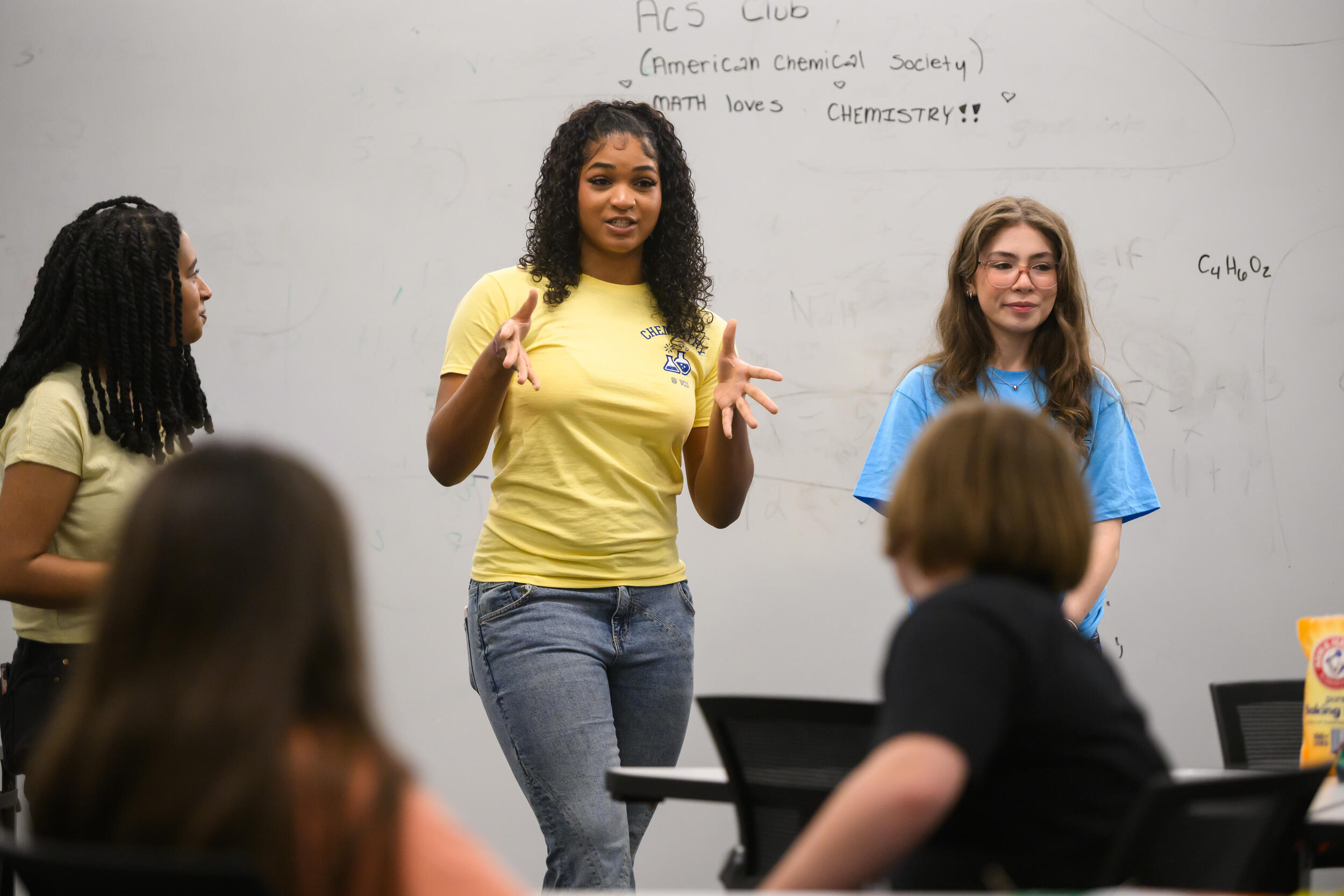 A photo of three women at the front of a classroom with a white board behind them. 