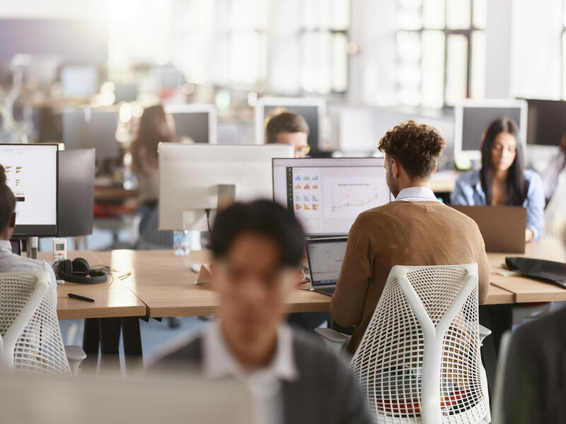 A photo of an office full of people sitting at desks with computers. 
