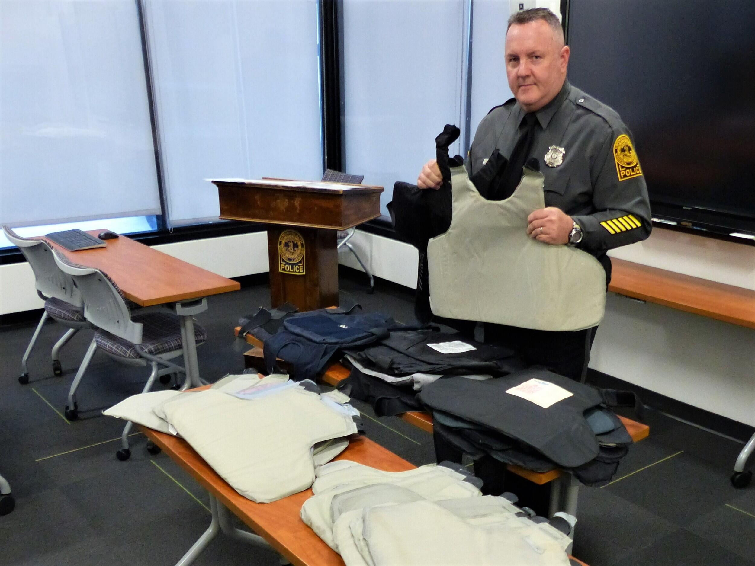 A VCU Police officer holding up ballistic vest panels in front of a table with more of them