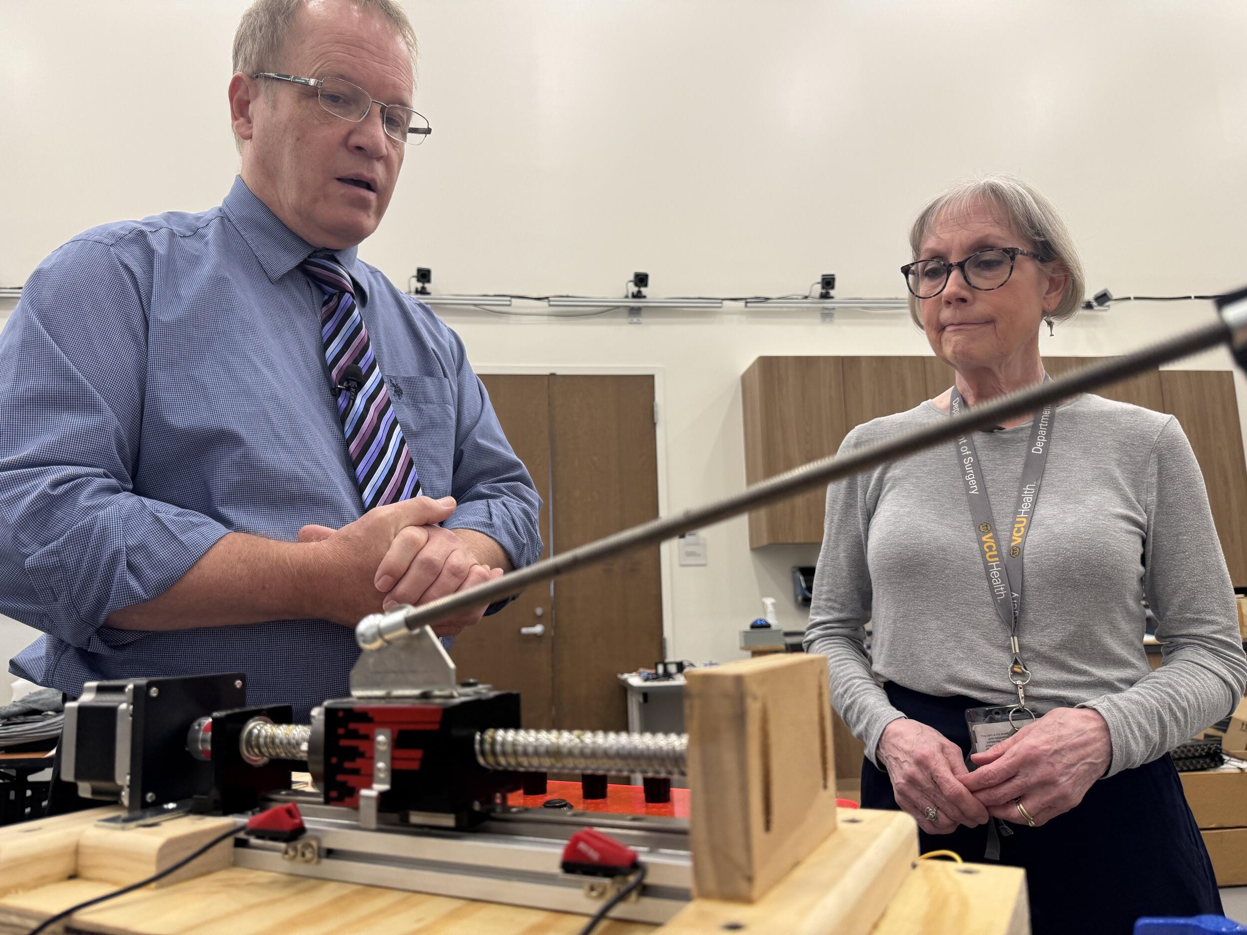 A photo of a man and woman looking at a mechanical object sitting on a table. 
