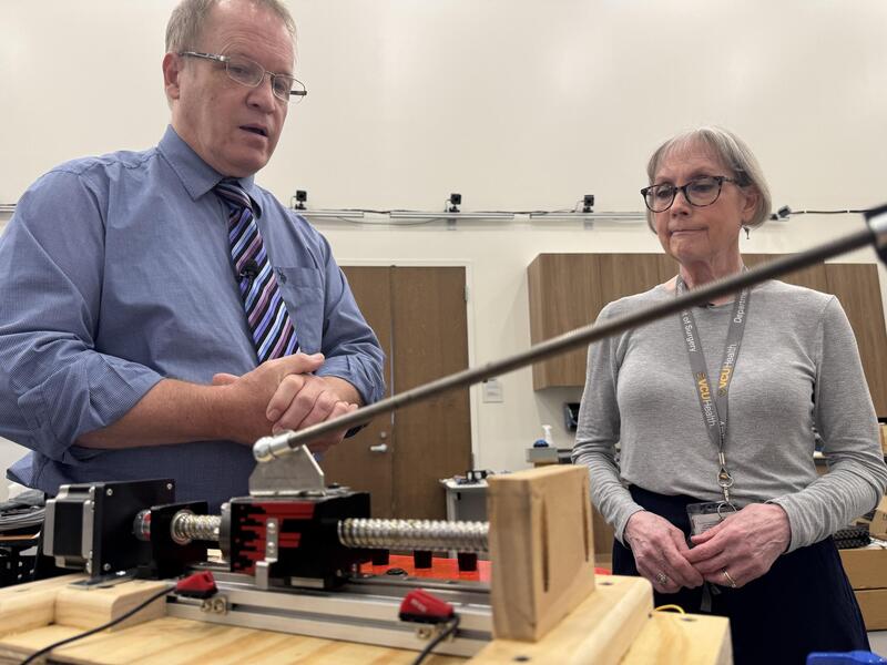 A photo of a man and woman looking at a mechanical object sitting on a table. 
