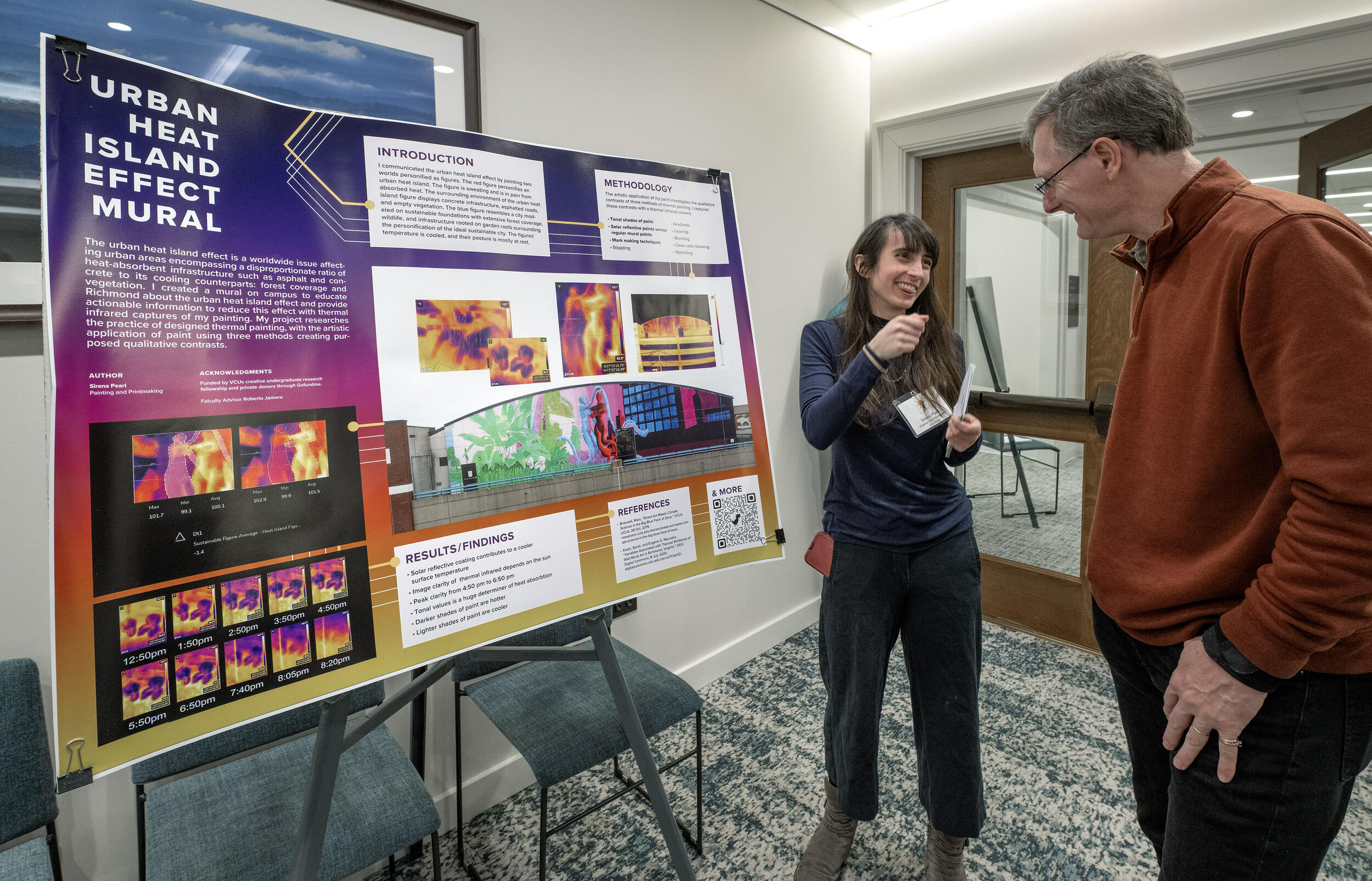 A photo of a woman standing to the right of a poster with research on it. She is laughing with a man who is standing in front of her. 