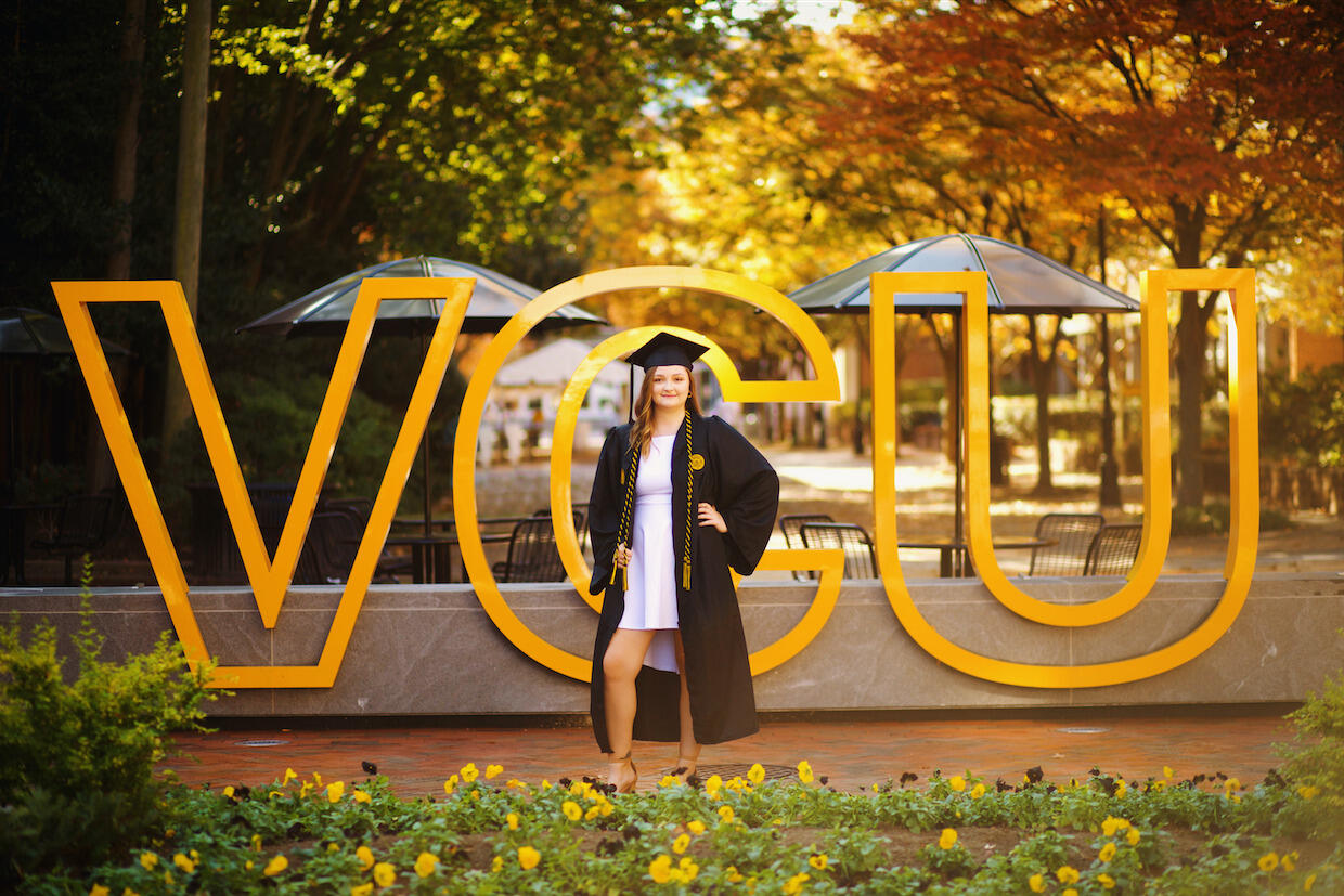 Sabrina Layne Odell, a first-generation college student, standing in front of \"V C U\" letters on campus, while wearing her cap and gown.