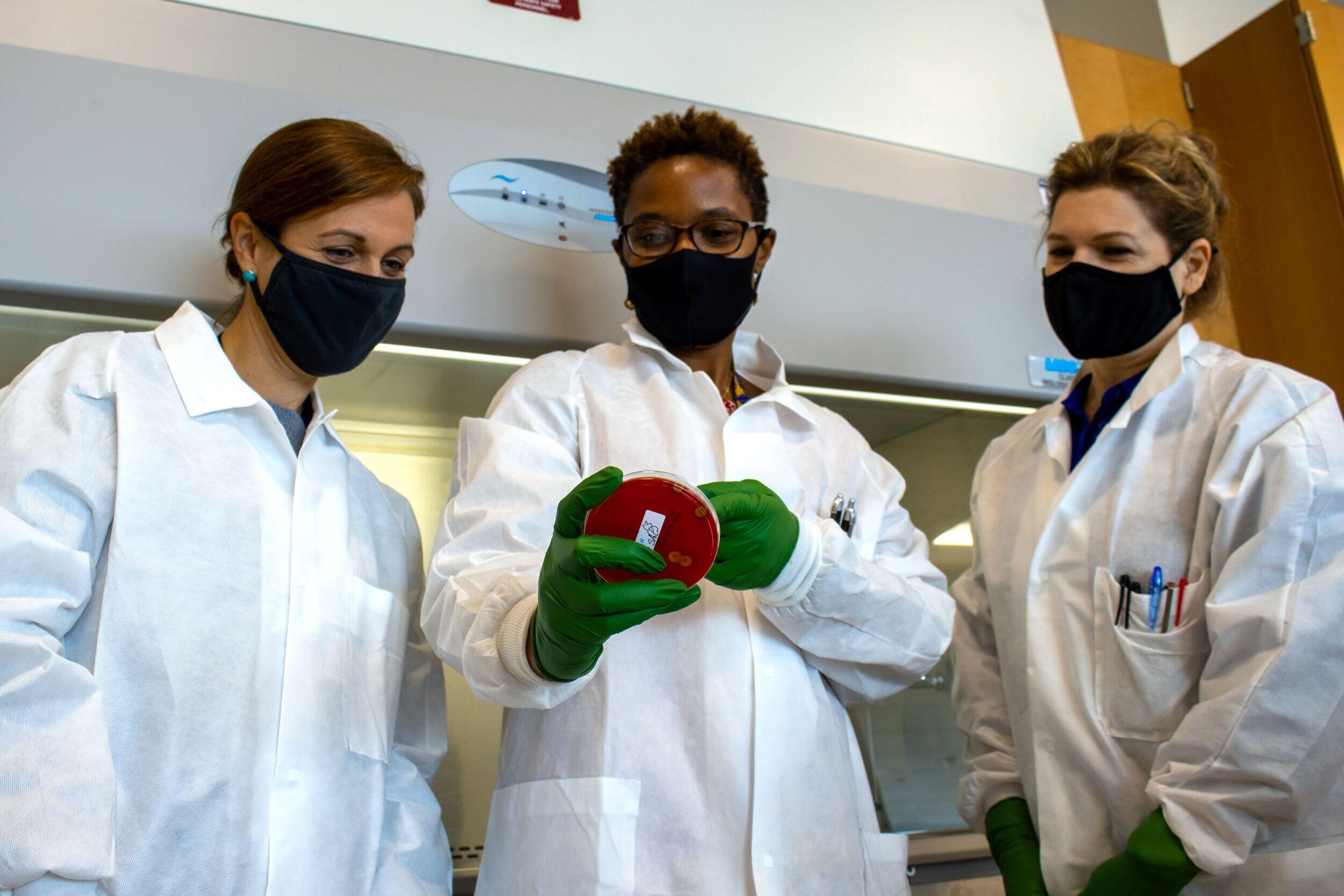 Three women in lab coats examine a sample.